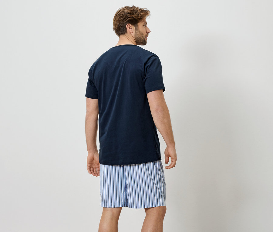 Mann von hinten in einem marineblauen T-Shirt und gestreiften Boxershorts vor einem weißen Hintergrund.