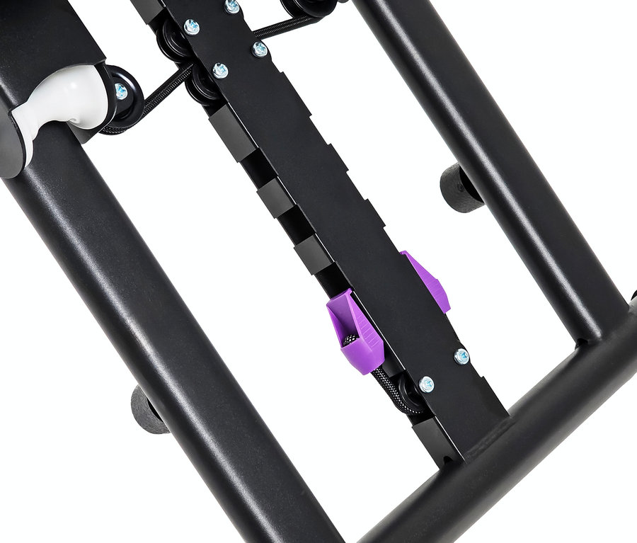 Detailaufnahme der Unterseite eines schwarzen Metallrahmens mit Rollen, Riemen und einer lila Klammer.