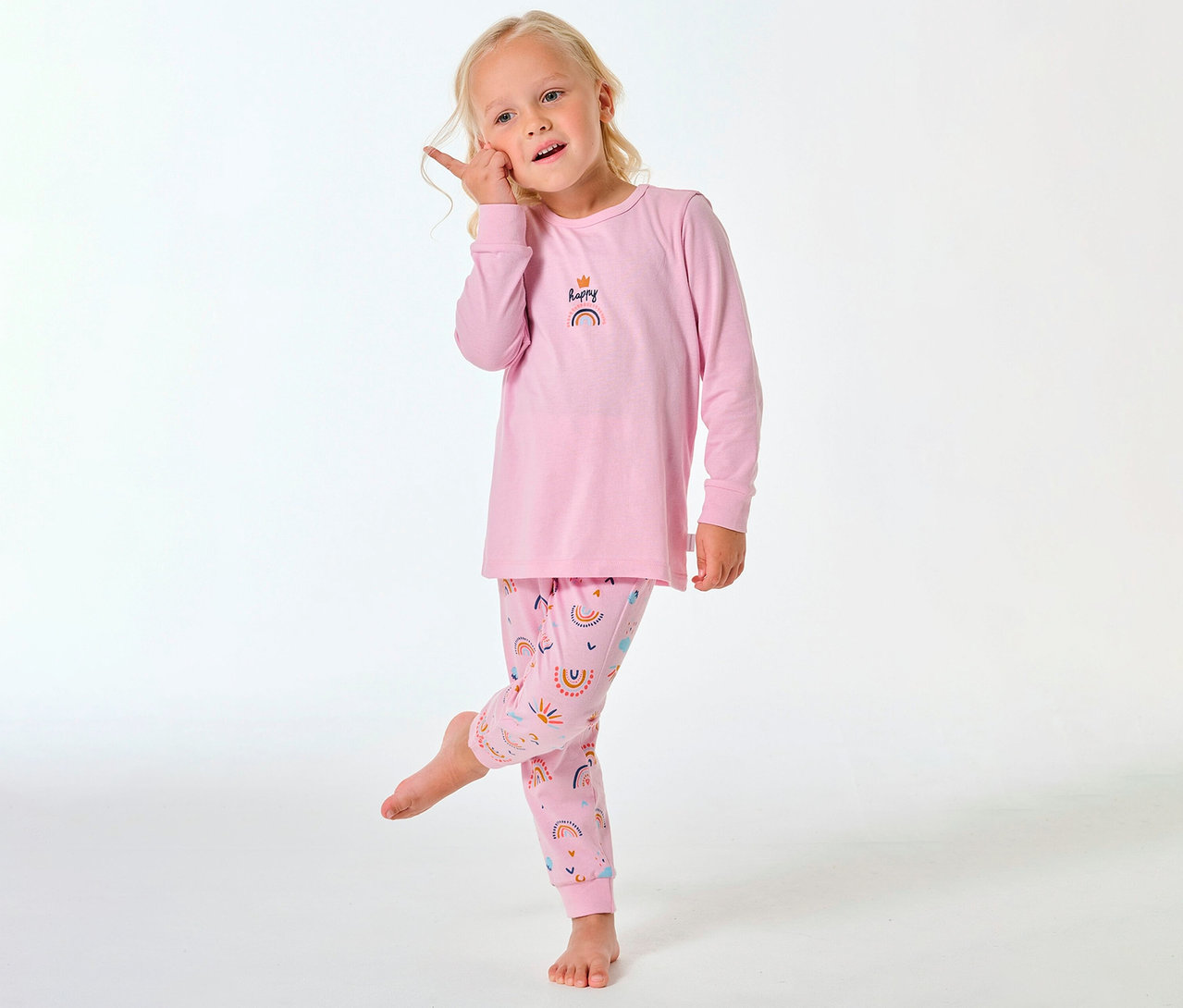 Mädchen in einem langen SCHIESSER Kinder-Pyjama mit Regenbogenmuster auf Hose und Oberteil.