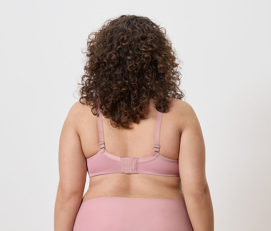 Rückansicht einer Frau mit lockigem Haar, die einen rosa BH trägt.