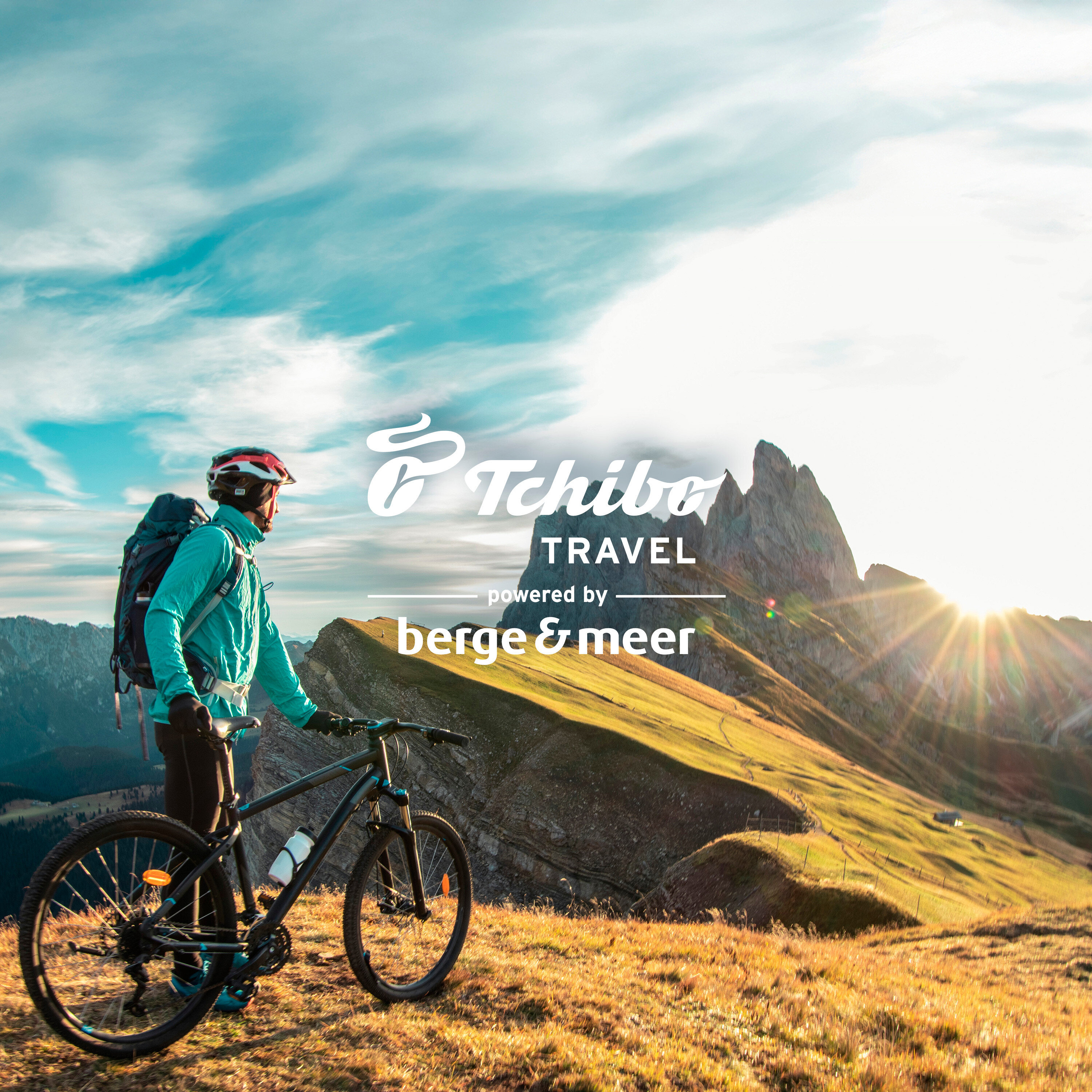 Radfahrer mit Rucksack und Helm steht neben Fahrrad auf einem Hügel mit Blick auf die Berge.