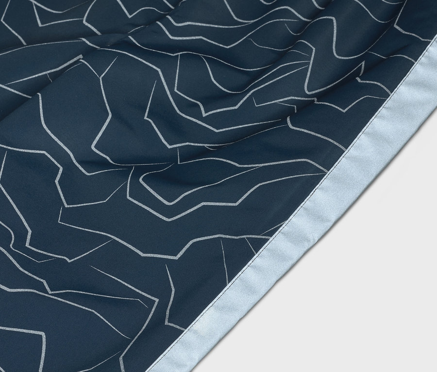 Nahaufnahme von marineblauem Stoff mit abstraktem, weißem Linienmuster und silberfarbenem Saum.