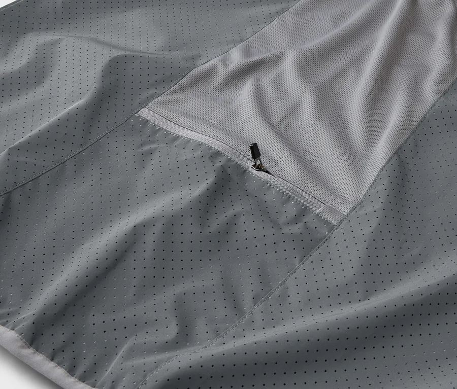 Nahaufnahme einer grauen Jacke mit Reißverschlusstasche und atmungsaktivem Mesh-Einsatz.