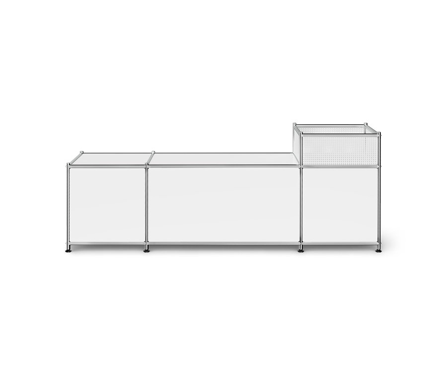 Ein weißes modulares Aufbewahrungsmöbel mit Chromrahmen, bestehend aus drei Elementen. Der linke Teil ist ein kleiner Schrank, der mittlere ein breiterer Schrank und der rechte Teil hat oben einen perforierten Metallkorb.