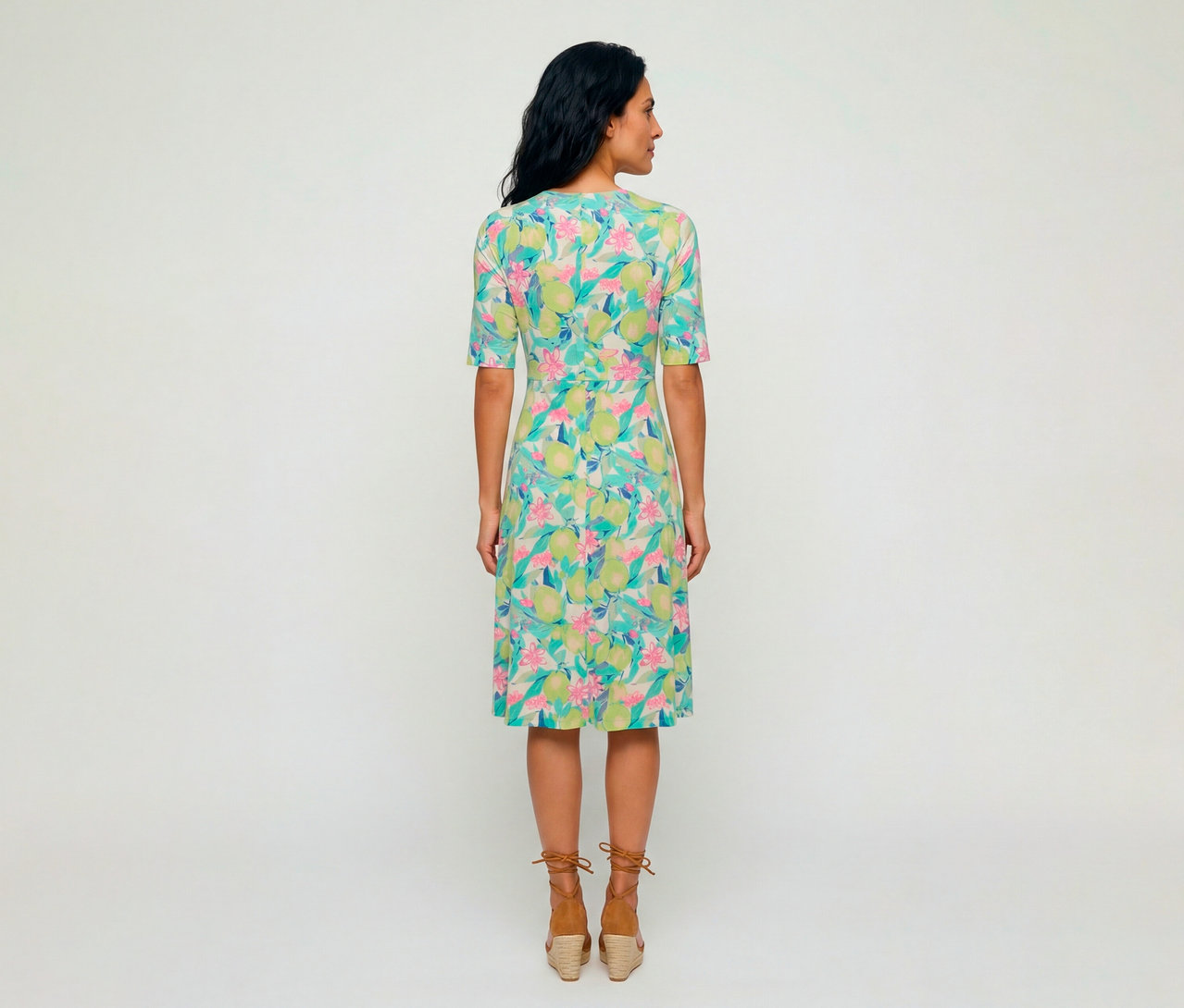 Frau von hinten in einem Olsen Jerseykleid mit buntem Muster aus grünen Zitronen und rosa Blüten, dazu braune Espadrille-Keilsandalen.