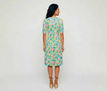 Frau von hinten in einem Olsen Jerseykleid mit buntem Muster aus grünen Zitronen und rosa Blüten, dazu braune Espadrille-Keilsandalen.