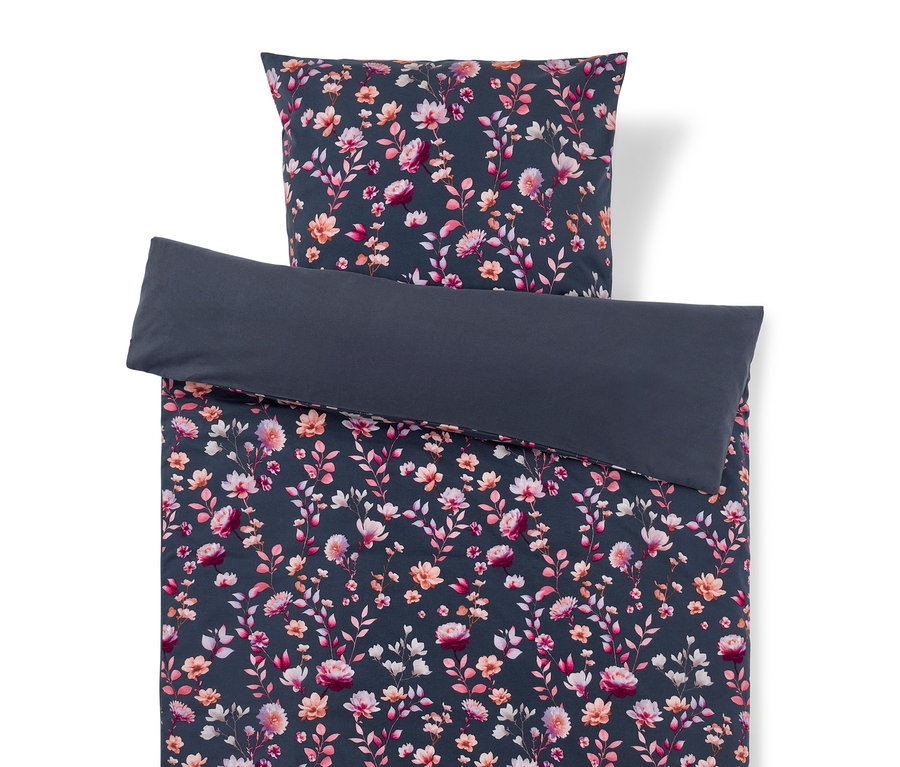 Bettwäsche-Set mit dunkelblau/grauem Blumenmuster in Rosa, Pfirsich und Weiß. Der Bettbezug ist umgeschlagen und zeigt eine einfarbige dunkelblau/graue Unterseite, der Kissenbezug liegt oben.