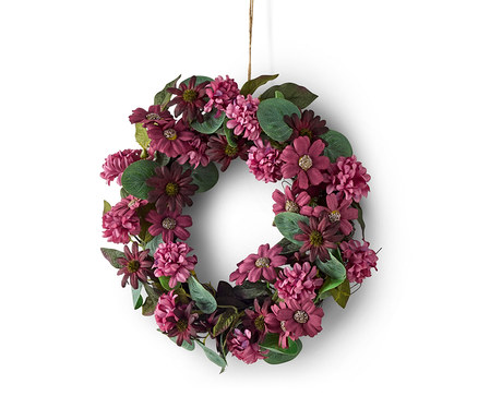 Blumenkranz aus lila und bordeauxroten Blüten und grünen Blättern, an einer Schnur vor weißem Hintergrund hängend.