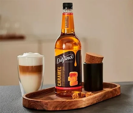 Ein Glas Getränk steht neben einer Flasche DaVinci Karamell Sirup auf einem Holztablett.