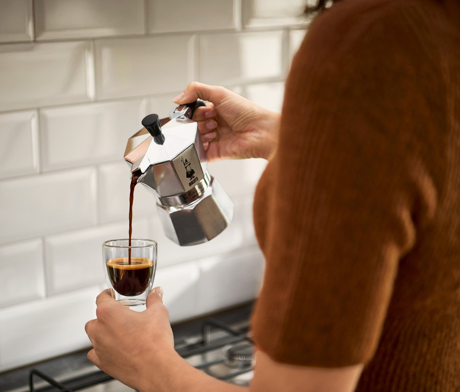Eine Person gießt Kaffee aus einer silbernen Espressokanne in ein Glas.