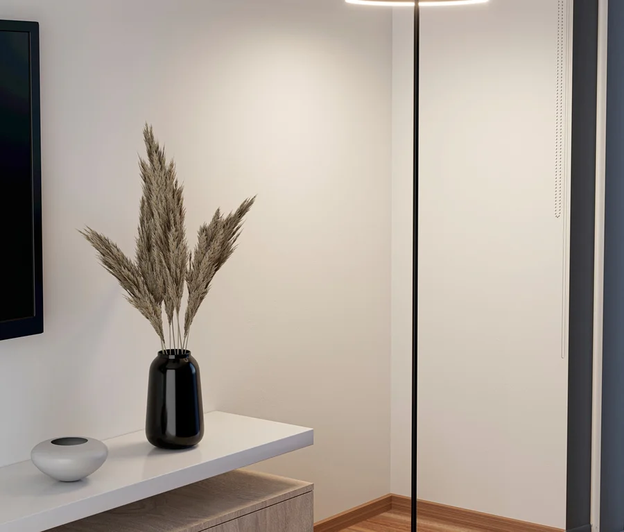 Moderne Stehlampe mit rundem, beleuchtetem Kopf in einer Zimmerecke, neben einem TV-Möbel mit Trockenpflanzen in einer Vase und einer Dekoschale.