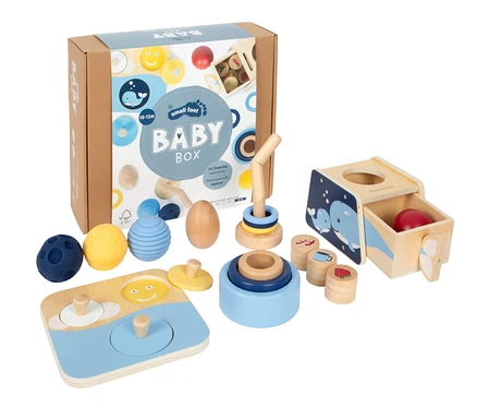 Eine Baby Box von Small Foot mit verschiedenen Holz- und Silikonspielzeugen, darunter Stapelringe, ein Steckpuzzle, Fühlbälle und eine Formensortierbox mit Walmotiv.