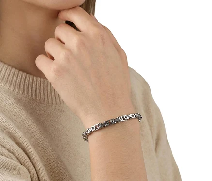 Frau trägt einen Amor Glieder-Armschmuck am linken Handgelenk und einen beigen Pullover.