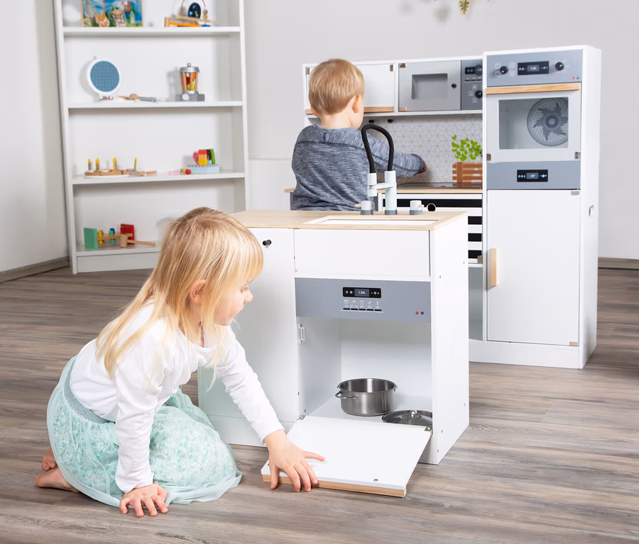 Mädchen spielt mit small foot Kinderküche modular XL, öffnet die Tür, in der sich ein Topf befindet.