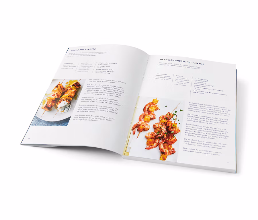 Kochbuch geöffnet auf einer Seite mit Rezepten für Lachs- und Garnelenspieße mit Ananas. Buch »Campingküche« sichtbar.
