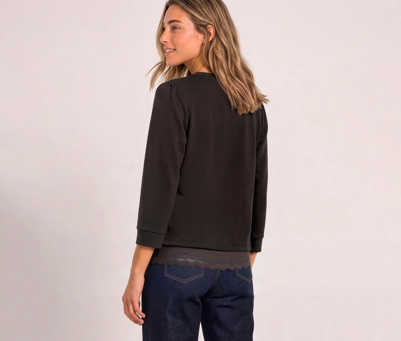 Eine Frau von hinten, die über ihre rechte Schulter blickt, trägt ein braunes Street One 3/4-Jerseyshirt mit Puffärmeln und eine dunkle Jeans.