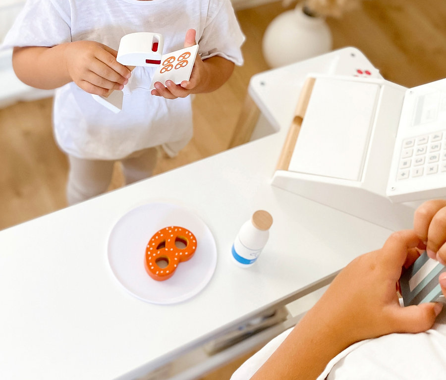 Mädchen hält Spielzeugkasse und Brezelkarte, während Junge an small foot Kasse »fresh« steht.