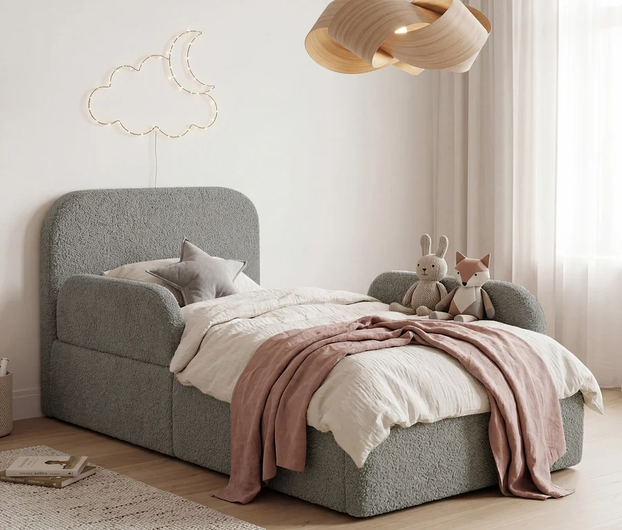 Ein Kinderzimmer mit einem grauen, strukturierten Bett mit weißer Bettdecke und rosa Überwurf, dazu ein Sternenkissen und Stofftiere. An der Wand hängen Wolken- und Mondlichterketten, eine Holzlampe hängt von der Decke.