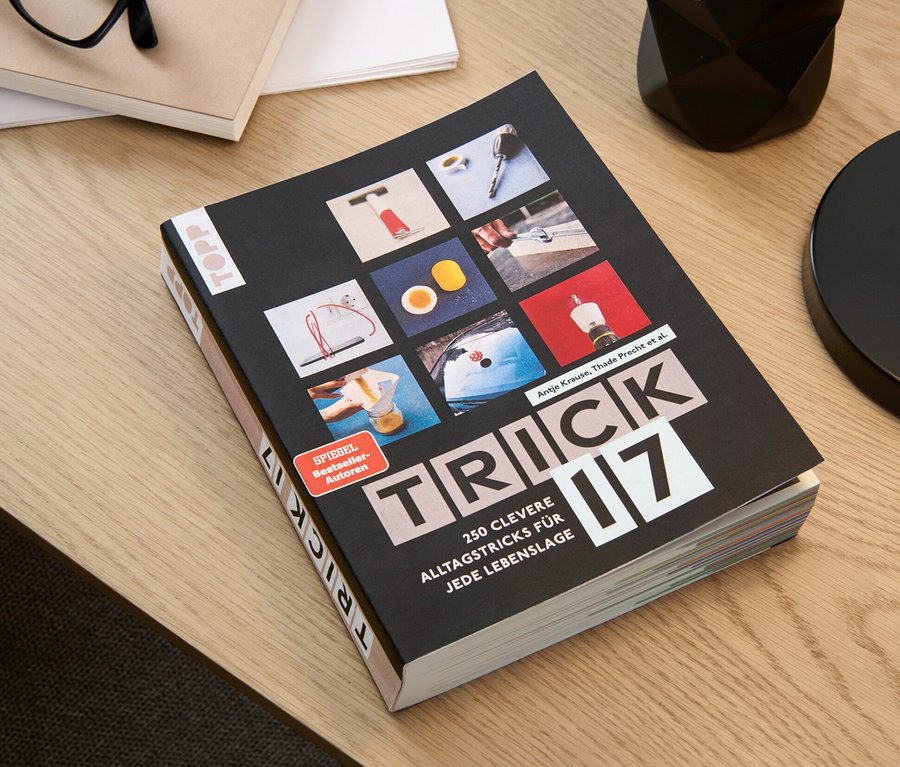 Das Buch "Trick 17" liegt auf einem Tisch neben einer Brille, einem Notizblock und einem Stifthalter.