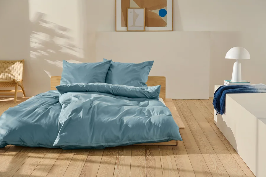 Blaue Baumwollsatin-Bettwäsche in Normal- und Übergröße auf einem Bett.