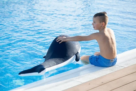 Junge sitzt am Pool und streichelt aufblasbaren Pool Buddy Wal.