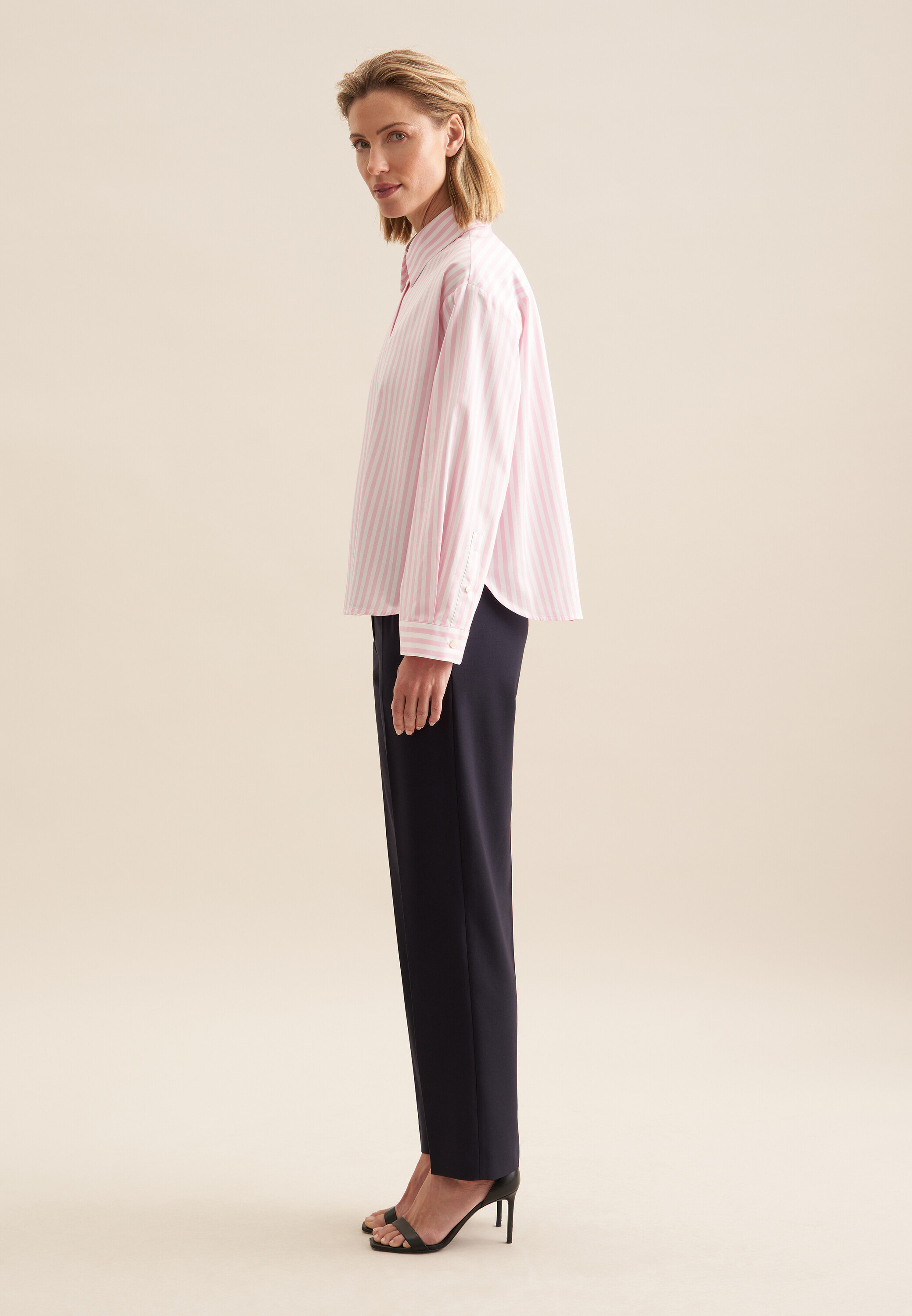 Frau posiert in rosafarbener Seidensticker Oversize Hemdbluse und dunkelblauer Hose.