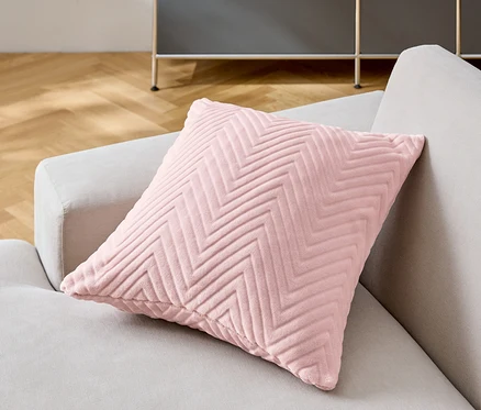 Ein rosa Zierkissen mit Chevron-Muster liegt auf einem grauen Sofa.
