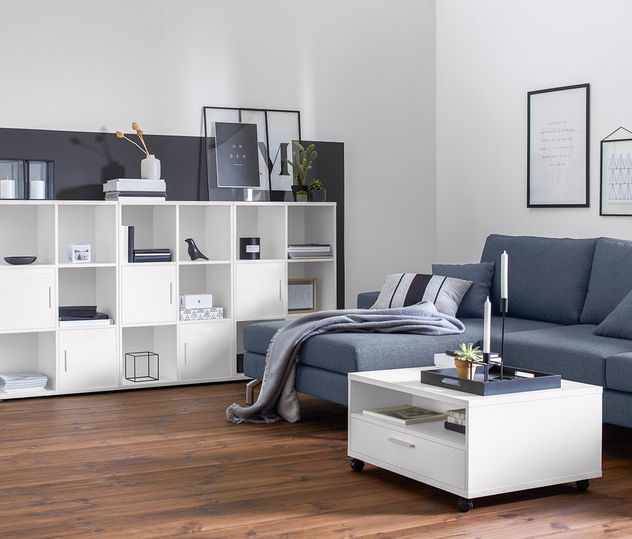 Wohnzimmer mit blau-grauem Max Winzer® Ecksofa, Longchair links, Stauraum-Couchtisch auf Rollen und offenem Regal mit 2 geschlossenen Fächern.