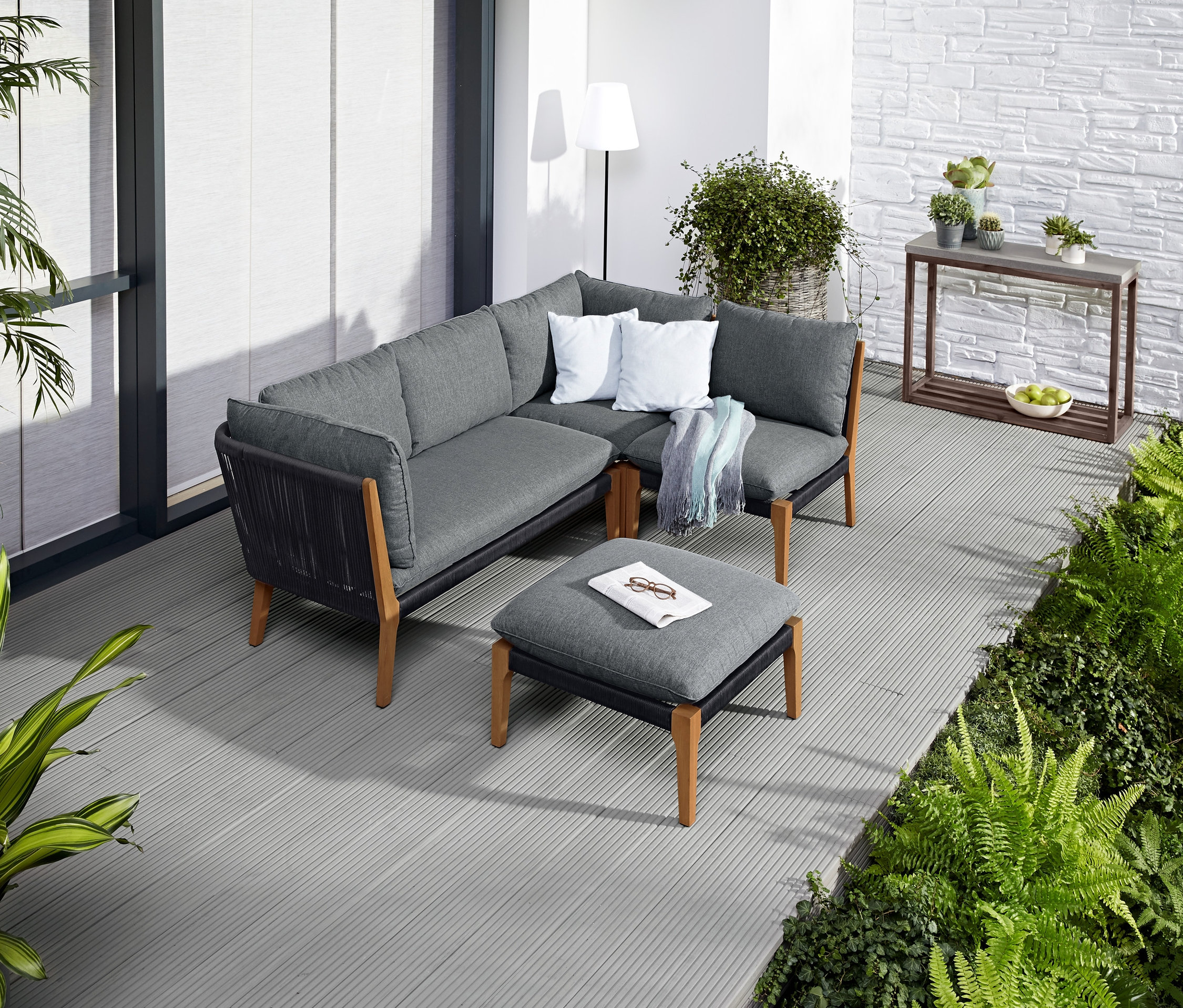 Eine Eckcouch und ein Hocker stehen auf einer Terrasse neben einer LED-Outdoor-Stehleuchte.