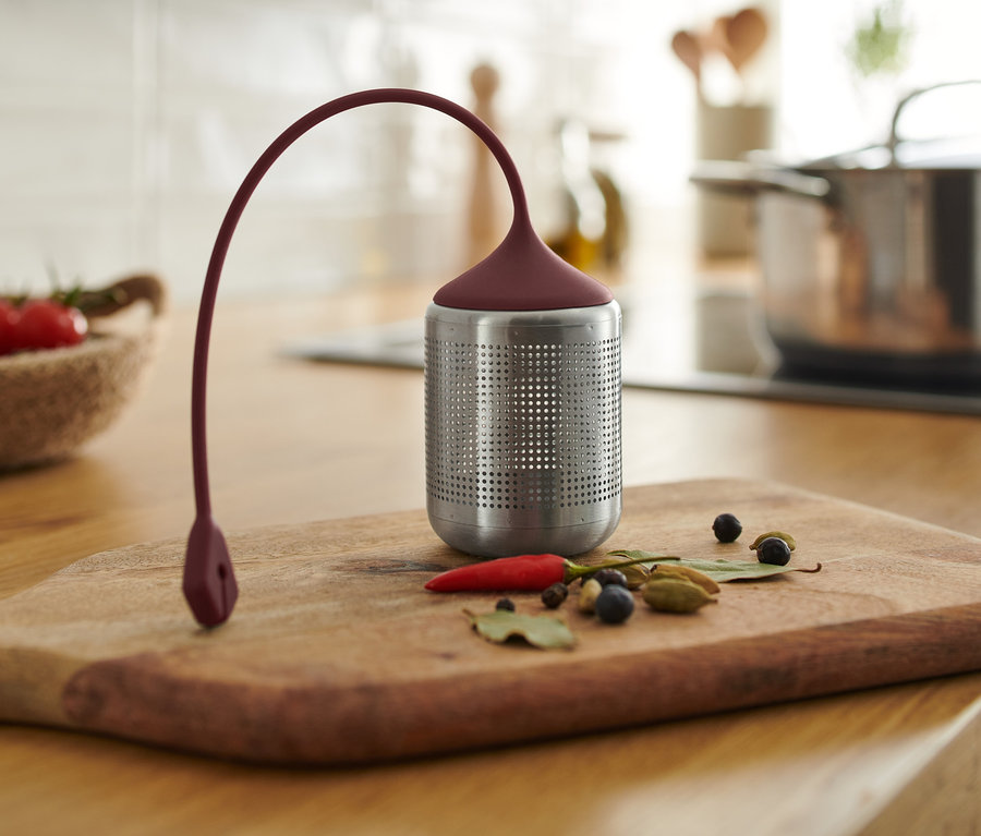 Ein Gewürzsieb steht mit Gewürzen auf einem Holzbrett.