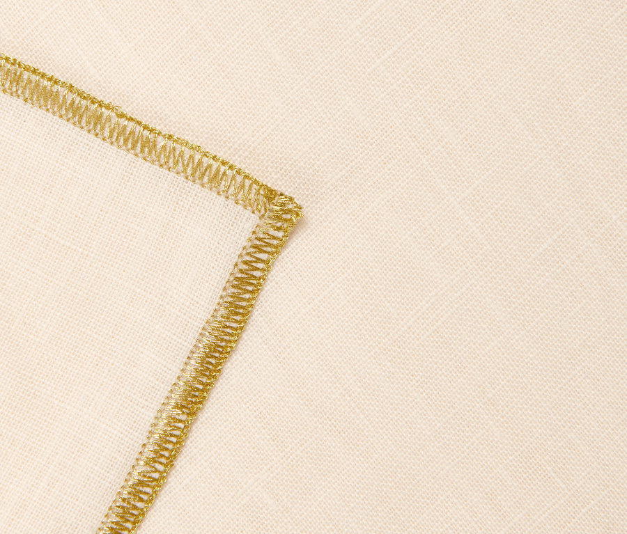 Detailaufnahme einer cremefarbenen Leinen-Tafeldecke mit goldenem Zierstich.