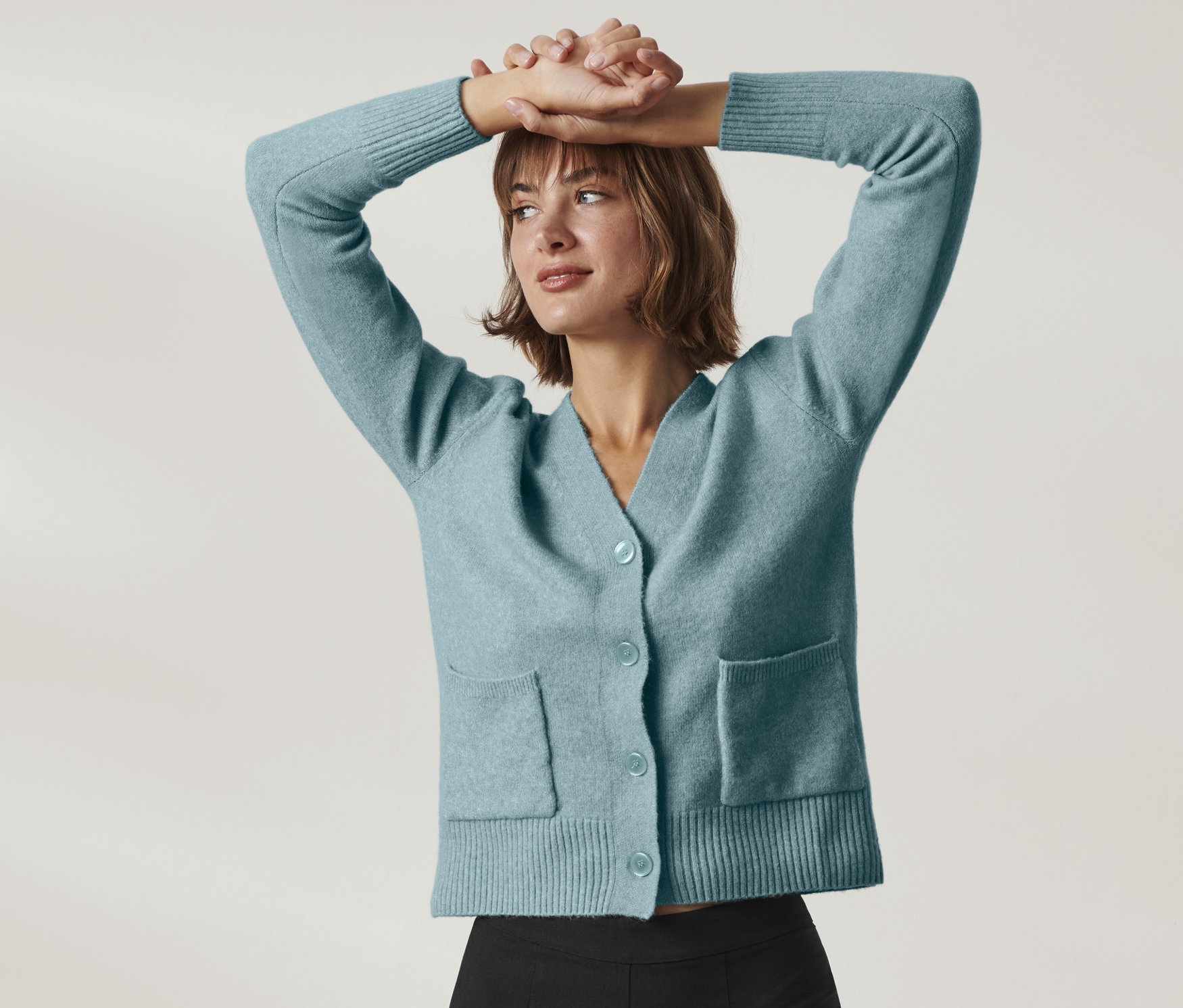 Frau posiert mit den Händen über dem Kopf in einer Strickjacke mit Wolle.