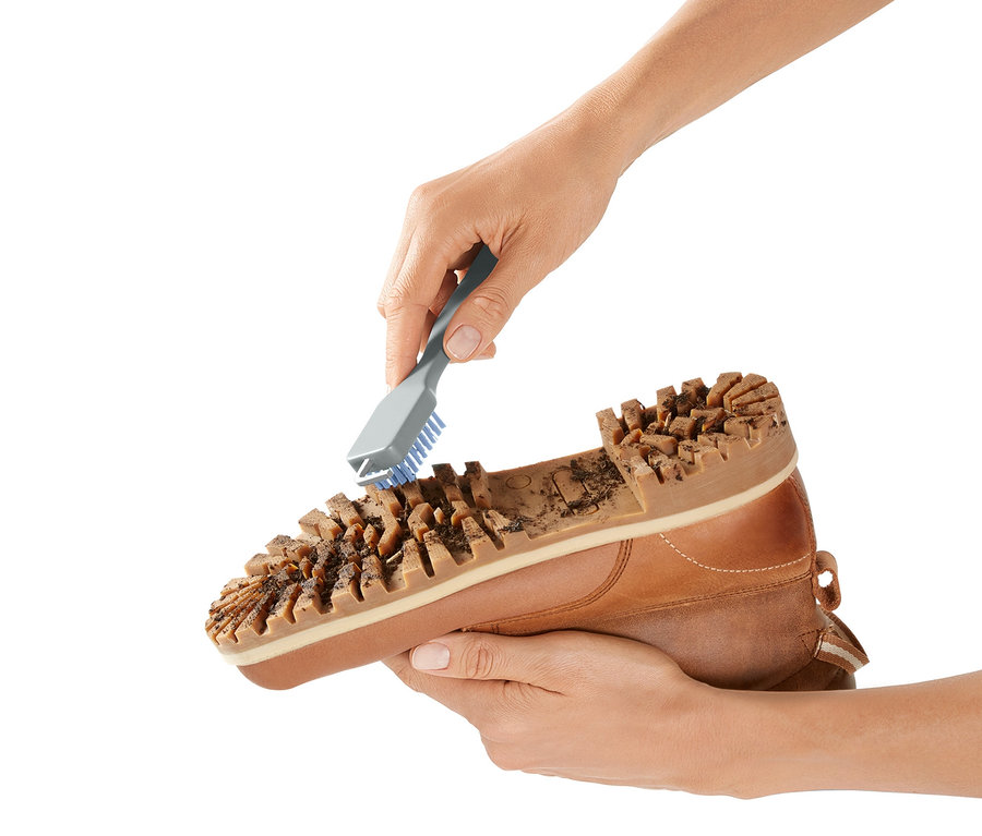 Eine Hand reinigt die Sohle eines braunen Schuhs mit einer Schuhsohlen-Reinigungsbürste.