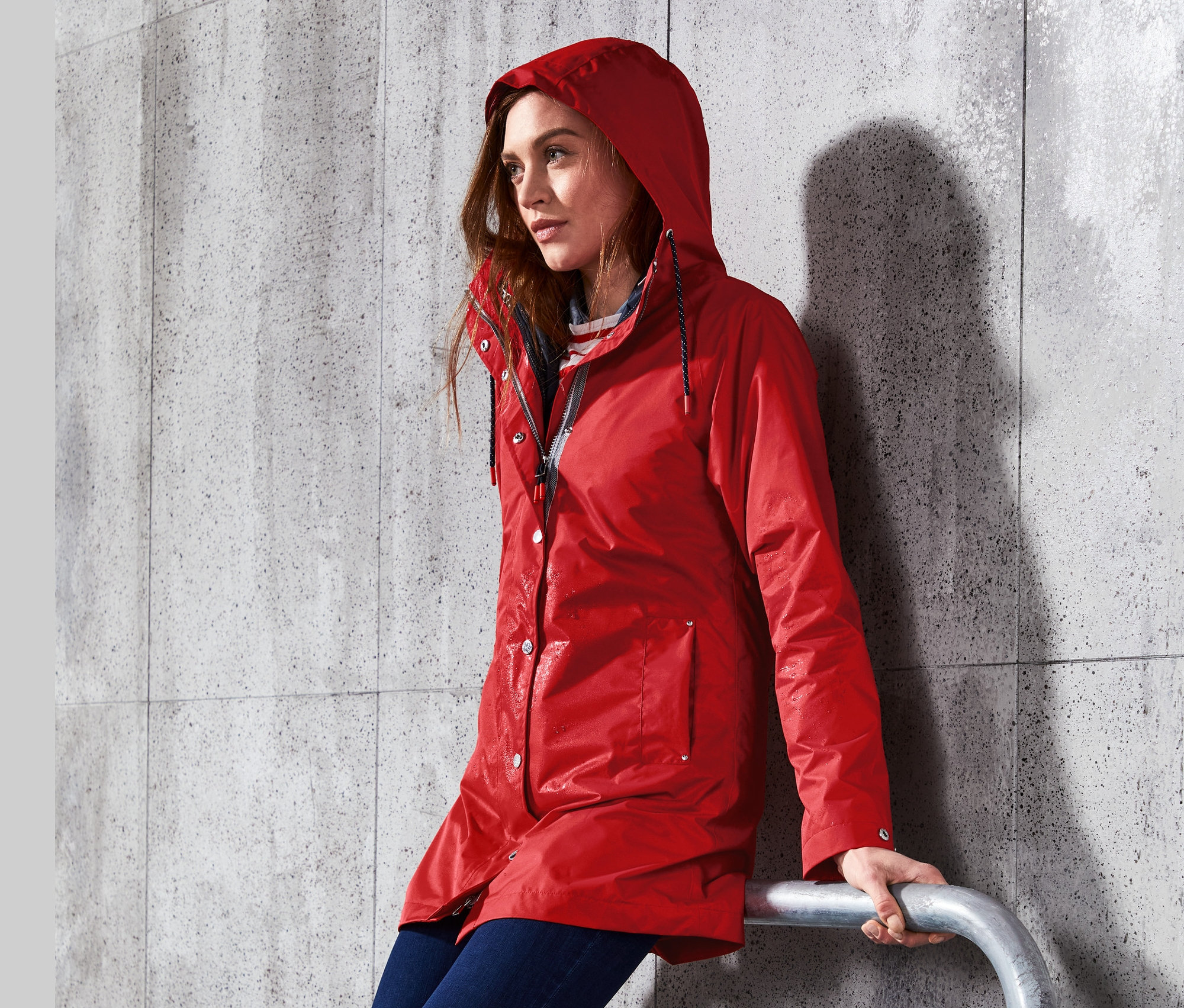 Frau sitzt an ein Geländer gelehnt und trägt eine rote 3-in-1-Regenjacke.