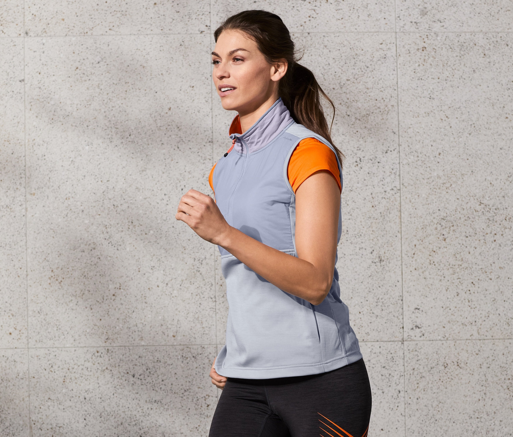 Frau mit grauer Laufweste und Leggings mit orangen Streifen läuft.