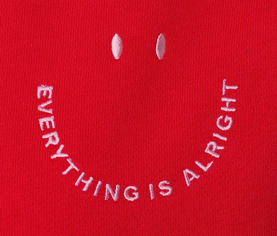 Detailansicht eines roten Hoodies mit aufgestickertem Smiley.