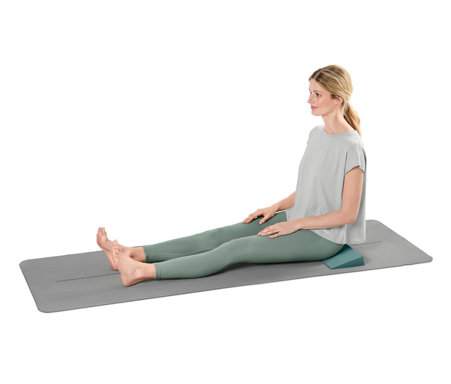 Frau sitzt mit Yoga-Wedge unter dem Gesäß auf einer Yoga-Matte.