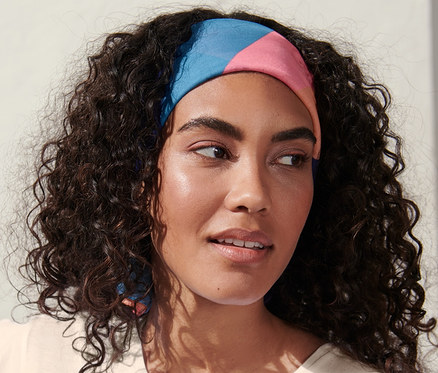 Frau mit dunklen, lockigen Haaren trägt ein sommerliches Halstuch.