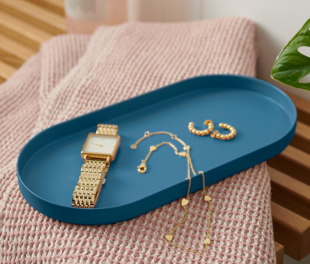 Auf einer Bank liegt ein blaues Tablett aus Metall mit einer Uhr und Schmuck.