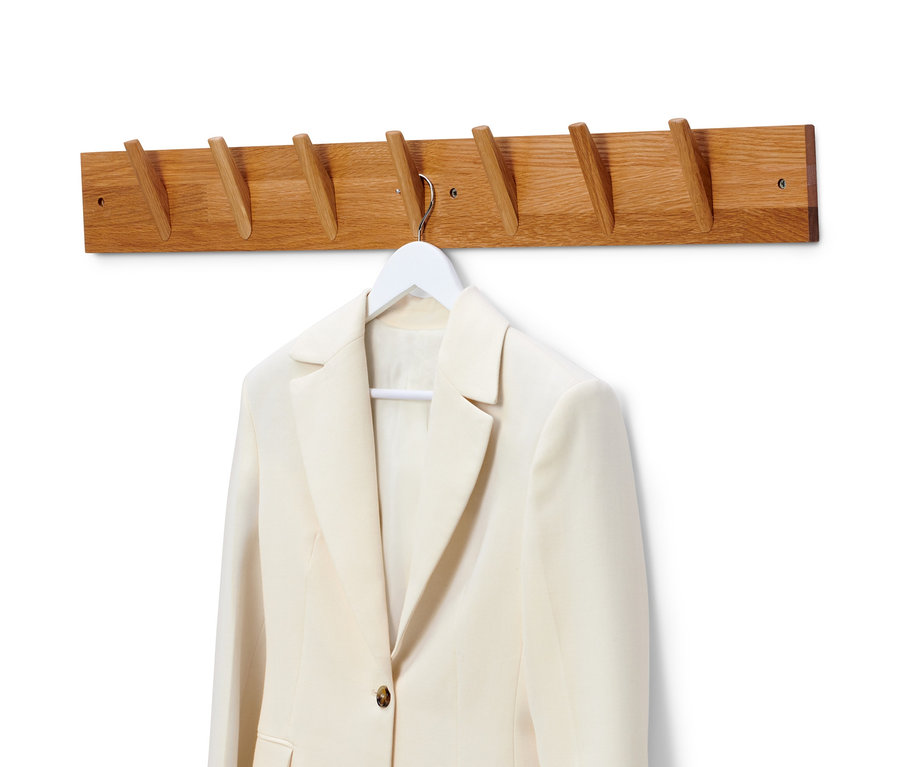 Ein beige Blazer hängt an einem weißen Bügel an einer Wandgarderobe aus Massivholz.