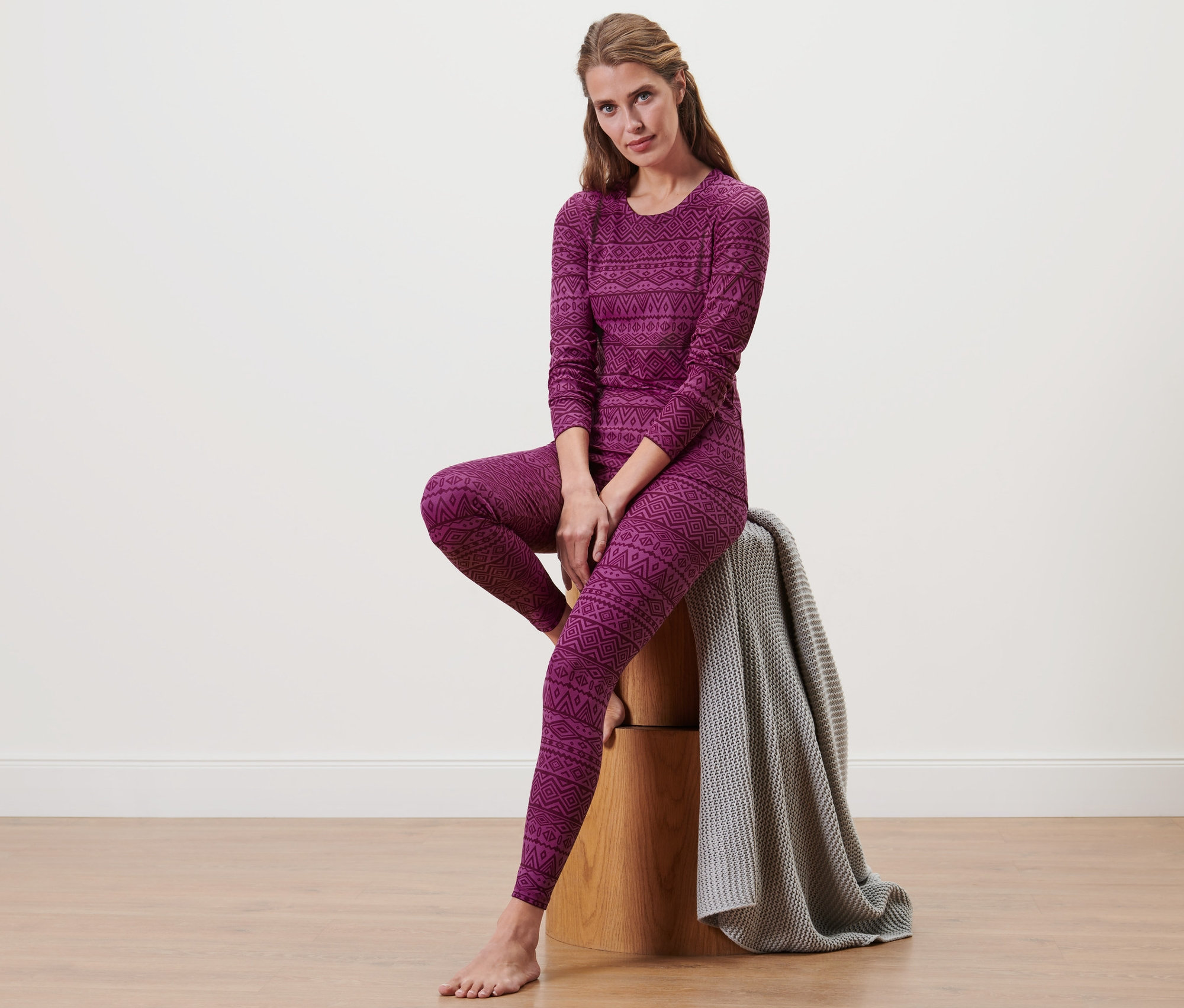 Frau sitzt auf einem Holzhocker und trägt Thermo-Funktionsunterwäsche.