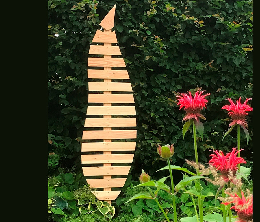 Eine Rankhilfe »Bambus« steht in einem Garten mit roten Blumen.