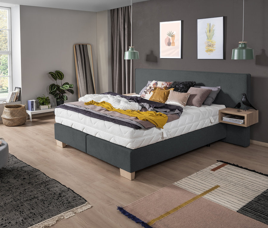 Schlafzimmer mit grauem Boxspringbett "DAVINA", Nachttisch und Dekoration.