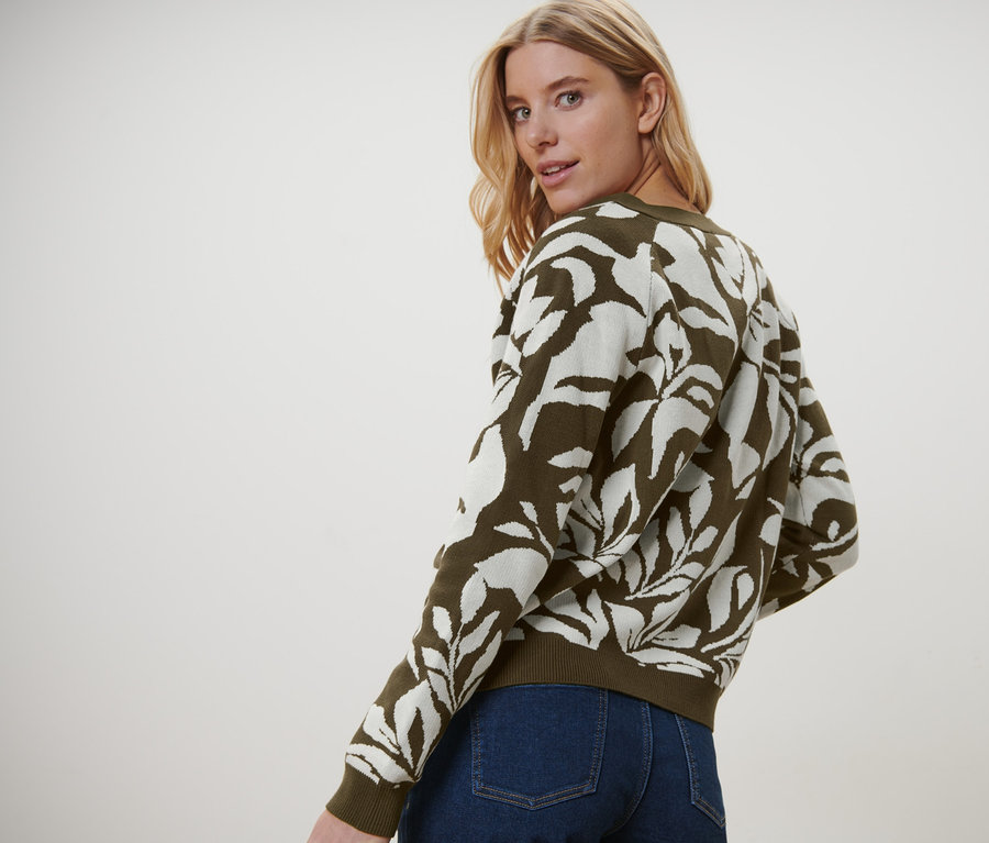 Blonde Frau blickt über die Schulter und trägt einen Grobstrick-Cardigan mit Jacquard und Jeans.