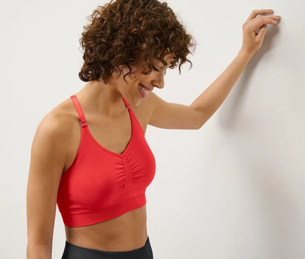 Frau lehnt an Wand und trägt rotes Seamless-Sport-Bustier.