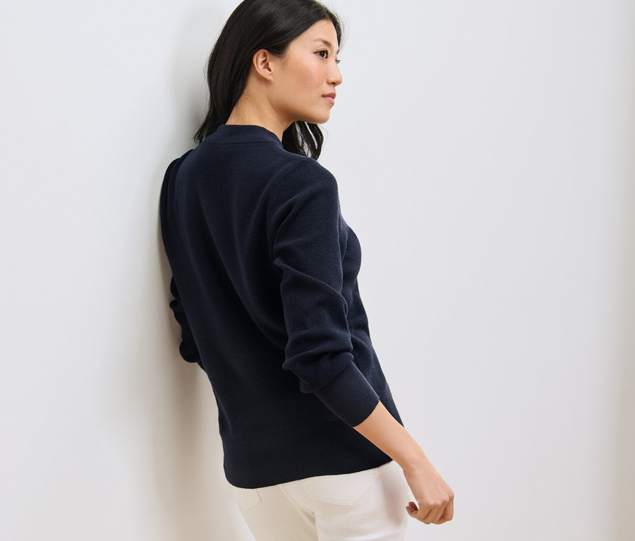 Frau lehnt an Wand, trägt dunkelblauen Feinstrickpullover.