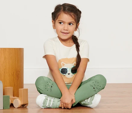 Mädchen sitzt am Boden und trägt 2 Kinder-Leggings und ein Löwen-T-Shirt.