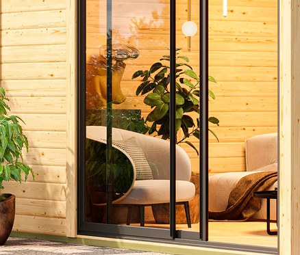 Innenansicht des Karibu Saunahauses »Linda Bio« mit Sesseln und Pflanzen hinter einer Glastür.