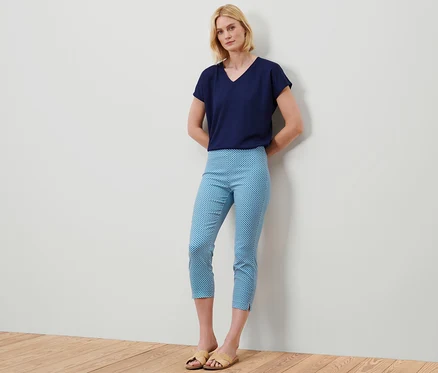 Frau steht und trägt ein blaues T-Shirt und eine 7/8-Stretchhose mit Alloverprint.