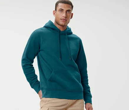 Mann posiert vor hellem Hintergrund in petrolfarbenem Hoodie.